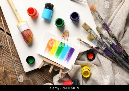 Leinwand mit Bürsten, Farben und Lappen auf braunem Holztisch Stockfoto