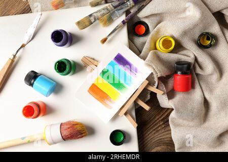 Leinwand mit Bürsten, Farben und Lappen auf braunem Holztisch Stockfoto