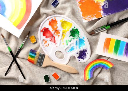 Künstlerpalette und Pinsel mit Farben und Zeichnungen auf Textilhintergrund Stockfoto