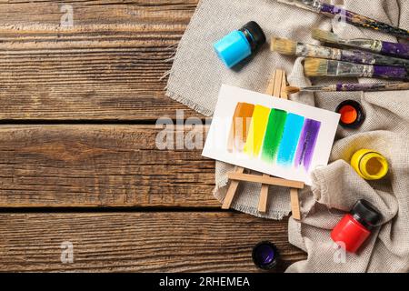 Mini-Staffelei mit Farben, Bürsten und Tuch auf braunem Holzhintergrund Stockfoto