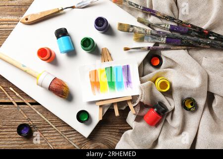 Leinwand mit Bürsten, Farben und Lappen auf braunem Holztisch Stockfoto