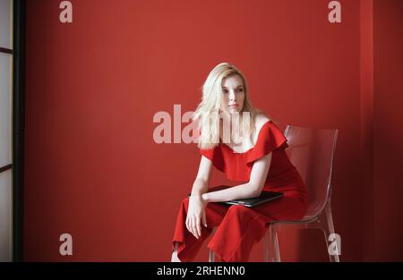 Junge Erwachsene Frau sitzt auf einem Stuhl und hält Laptop Stockfoto