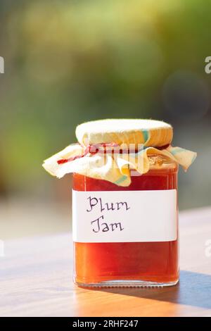 Ein Glas hausgemachte Pflaumenmarmelade. Der Glasbehälter ist mit einem klaren, handschriftlichen Etikett versehen, und der Becher ist mit einem Tuch belegt Stockfoto