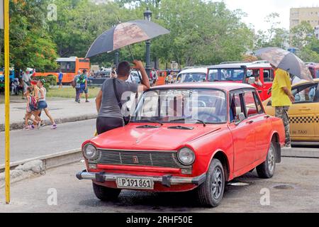 Havanna, Kuba, ein altes Auto, das als privates kleines Transportunternehmen im Stadtzentrum betrieben wird. Menschen mit Sonnenschirmen zum Schutz vor Sonnenlicht. Stockfoto
