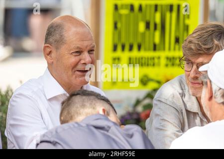 Düsseldorf, Deutschland. 16. Aug. 2023. Bundeskanzler Olaf Scholz (L, SPD) spricht vor einem Büdchen mit den Worten Büdchentag auf einem Plakat im Hintergrund zu Düsseldorfer Bürgern. Die Düsseldorfer Büdchentag hat die Einladung herausgegeben. Kredit: Christoph Reichwein/dpa/Alamy Live News Stockfoto