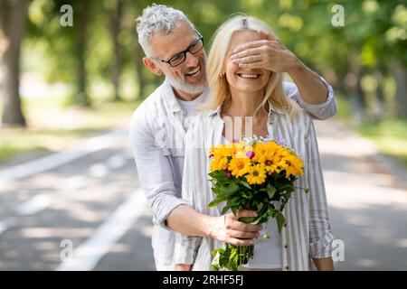 Liebender Reifer Ehemann Überraschende Frau Mit Blumen, Augen Bedeckend Und Blumenstrauß Gebend Stockfoto