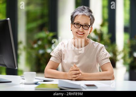 Porträt einer fröhlichen Reifen Frau, die am Arbeitsplatz mit dem pc sitzt Stockfoto