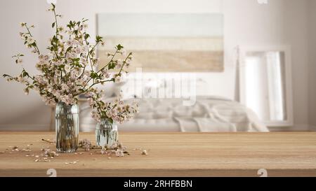 Holztisch, Schreibtisch oder Regal mit Kirschblütenzweigen in Glasvase und verschwommener Sicht auf das böhmische Schlafzimmer mit Doppelbett, Boho Interi Stockfoto