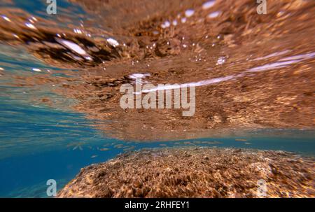 Unterwasseransicht. Kleine Fische in der Nähe der Felsen und Reflexionen im Wasser. Stockfoto