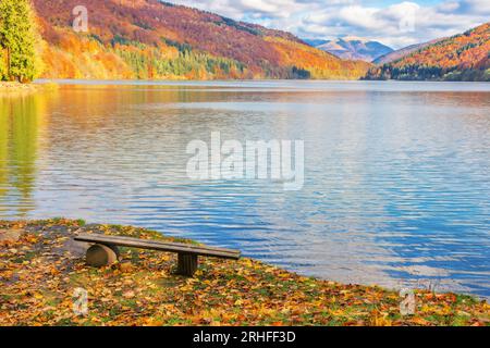 Holzbank am Ufer eines Tereblya-Wasserreservats. Bunte Landschaft der karpaten an einem sonnigen Tag im Herbst. Reise- und Entspannungsempfang Stockfoto