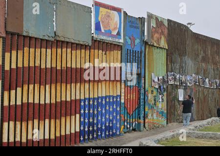 Tijuana, Baja, Kalifornien, Mexiko. 15. Aug. 2023. Ein Stück der gefallenen Berliner Mauer, gespendet an die Stadt Tijuana. Der Bruchteil der Mauer wird dauerhaft am Grenzzaun am Strand ausgestellt, wo derzeit von den Vereinigten Staaten ein bis zu 30 Meter hoher Ersatzzaun gebaut wird, der San Diego, Kalifornien und Mexiko teilt. Ein Wandgemälde aus Protest gegen die Dekonstruktion des Freundesschaftsparks, das Donald Trump und US-Präsident Joe Biden beim Küssen zeigt, ist an der Wand zu sehen. Es ist ein Vergleich des Originalbildes, das Leonid Breschnew, Führer der UdSSR und Erich Honecke, darstellt Stockfoto