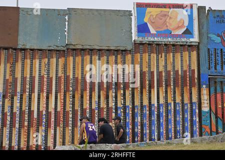 Tijuana, Baja, Kalifornien, Mexiko. 15. Aug. 2023. Ein Stück der gefallenen Berliner Mauer, gespendet an die Stadt Tijuana. Der Bruchteil der Mauer wird dauerhaft am Grenzzaun am Strand ausgestellt, wo derzeit von den Vereinigten Staaten ein bis zu 30 Meter hoher Ersatzzaun gebaut wird, der San Diego, Kalifornien und Mexiko teilt. Ein Wandgemälde aus Protest gegen die Dekonstruktion des Freundesschaftsparks, das Donald Trump und US-Präsident Joe Biden beim Küssen zeigt, ist an der Wand zu sehen. Es ist ein Vergleich des Originalbildes, das Leonid Breschnew, Führer der UdSSR und Erich Honecke, darstellt Stockfoto