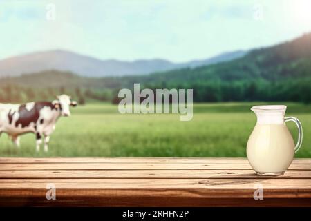 Frische Milch auf rustikalem Tisch vor verschwommenem Hintergrund mit Kuh auf Wiese Stockfoto