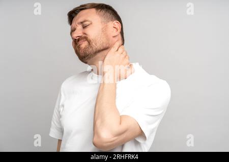 Der Mann leidet unter Nackenschmerzen isoliert auf Studiograuhintergrund. Halsschmerzen, Hernienkonzept Stockfoto