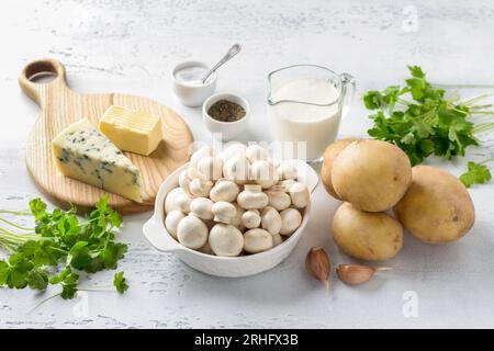 Frische Kartoffeln, Champignon-Pilze, Sahne, Butter, Blauschimmelkäse, Knoblauch, Kräuter, Salz, schwarzer Pfeffer auf hellblauem Hintergrund. Zutaten für einen Feinkost Stockfoto