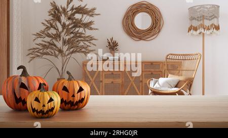 Halloween geschnitzte Kürbisse auf Holztisch. Herbstdekoration über Innenarchitektur-Szene. Böhmisches Wohnzimmer im Boho-Stil mit Rattanmöbeln Stockfoto