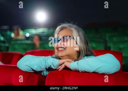 Ältere asiatische Frauen mit Brille sehen sich gern 3D-Filme und Popcorn in der Hand an und genießen das faszinierende Erlebnis. Stockfoto