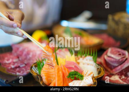 Eine Frau schwingt Stäbchen, um frischen Lachs Sashimi in einem japanischen Restaurant auf einen Teller zu legen und die Kunst des Essens einzufangen. Stockfoto