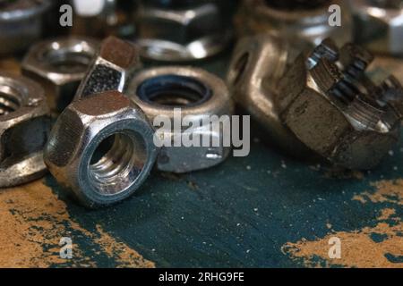Industrieller Reiz: Ein Haufen Metallnüsse auf einer alten Werkbank, betont durch einen Schlieren blauer Farbe. Perfekt für DIY-, Bau- oder mechanische Themen Stockfoto