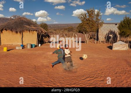 afrikanische Kinder spielen Fußball auf einem improvisierten Fußballfeld im Hof zwischen den reetgedeckten Hütten Stockfoto