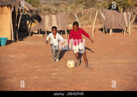 afrikanische Kinder spielen Fußball auf einem improvisierten Fußballfeld im Hof zwischen den reetgedeckten Hütten Stockfoto