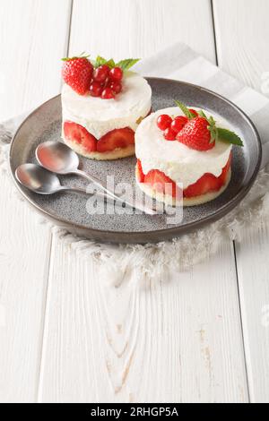 Französischer Mini Cake Fraisier mit frischen Erdbeeren und Johannisbeeren auf dem Teller auf dem Tisch. Vertikal Stockfoto