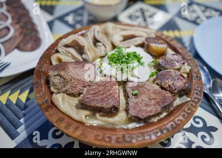 Traditionelles kasachisches asiatisches Gericht Beshbarmak: Nudeln mit Lamm und Zwiebeln, Nahaufnahme auf einem Teller auf dem Tisch. In der Nähe der Brühe in Schüsseln. dastarkhan. Bolied Stockfoto