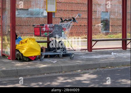 Ein obdachloser Mann mit seinen Habseligkeiten schläft in einer Bushaltestelle Stockfoto