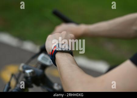 Abgeschnittenes Bild eines Radfahrers, der auf seinem Fahrrad sitzt und die Fortschrittsdaten der Sportaktivität auf der Smartwatch überprüft. Stockfoto