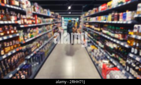 Defokussierte Ansicht des Gangs im Supermarkt mit Shopper und verschiedenen Lebensmitteln in den Regalen. Verschwommenes Foto für abstrakten Hintergrund. Stockfoto