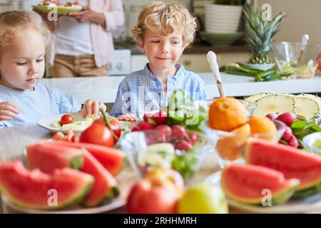 Blonder Junge, der neben der Schwester steht und zu Hause in der Küche Essen zubereitet Stockfoto