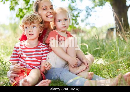 Porträt einer glücklichen Mutter, die mit Sohn und Tochter auf Gras im Garten sitzt Stockfoto
