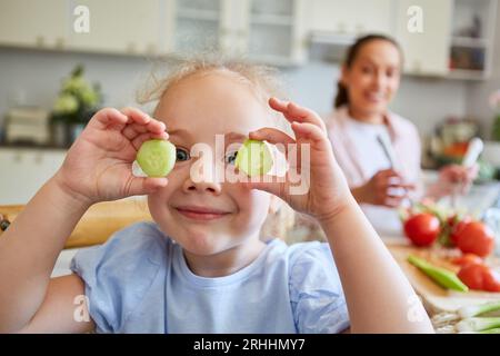 Porträt eines lächelnden Mädchens mit frischen Gurkenscheiben in der Küche zu Hause Stockfoto