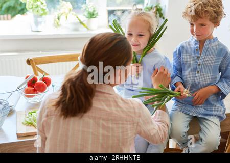 Mutter spricht mit Sohn und Tochter, die beim Zubereiten des Essens ein Sallion halten Stockfoto