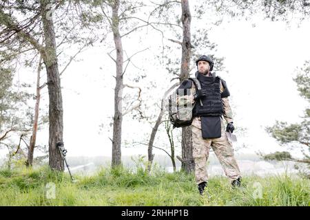 Ein junger Soldat in Uniformen und taktischer Weste arbeitet im Wald und bereitet sich auf die Aktion an einem temporären Waldstützpunkt vor. Ein Mann tut es bei der Minenräumung Stockfoto