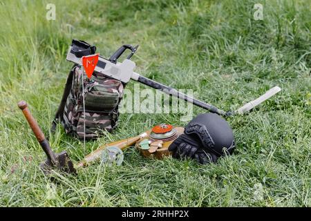 Sprengkörper und ein Metalldetektor liegen auf dem Hintergrund eines Waldmassivs. Ausrüstung für die Minenräumung des Gebiets. Stockfoto