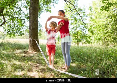 Mutter, die Sohn beim Slacklining im Garten unterstützt Stockfoto