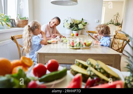 Glückliche Frau mit Sohn und Tochter, die zu Hause am Tisch sitzen Stockfoto