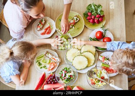 Mutter mit frischem Obst, Sohn und Tochter sitzen zu Hause am Tisch Stockfoto