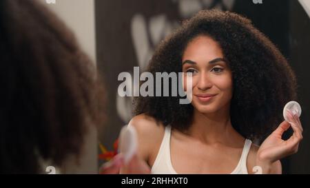 Spiegelreflektion weibliches Waschen des Gesichts mit Schwämmchen mizellares Wasser Tonic Gesichtspflege Beauty Routine afroamerikanische Frau Mädchen mit Wattepad Wischtuch Stockfoto