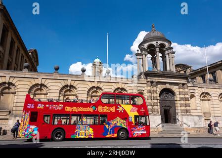 Ein Touristenbus mit offenem Oberdeck wartet vor dem Queen's College an der berühmten High Street von Oxford Stockfoto