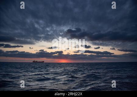 Farbenfroher roter und oranger Sonnenuntergang mit dunkelblauem Himmel im tiefblauen Meer mit Schiff im Hintergrund. Stockfoto