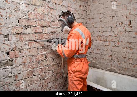 Männlicher Arbeiter, der Vollgesichts-Atemschutzmaske und Gehörschutz trägt, für Arbeiten in staubiger und lauter Umgebung bei Verwendung eines Schlagbohrers. Stockfoto