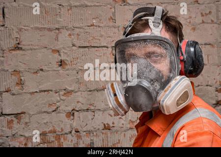 Bauarbeiter, der Vollmaske und Gehörschutz für Arbeiten in Gefahrenumgebungen trägt. Stockfoto