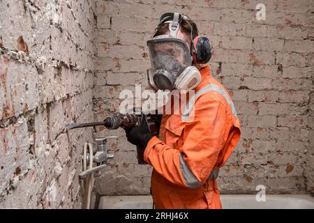 Bauarbeiter, der Vollgesichts-Atemschutzmaske und Gehörschutz für die Arbeit mit einem Bohrhammer trägt. Stockfoto