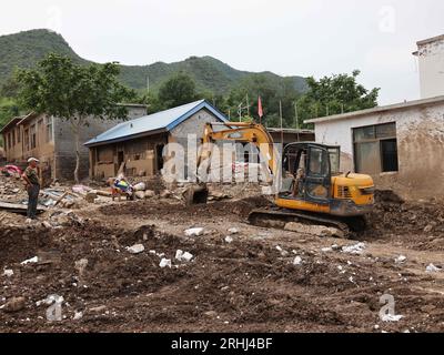 Baoding, chinesische Provinz Hebei. Aug. 2023. Ein Arbeiter fährt einen Bagger, um Schlamm im Dorf Pingyu im Laishui County in der nordchinesischen Provinz Hebei am 17. August 2023 aufzuräumen. Laishui County hat durch die Auswirkungen des Taifuns Doksuri in letzter Zeit starke Niederschläge erlitten. Die lokalen Behörden haben aktiv den Wiederaufbau nach Katastrophen durchgeführt, um die Sicherheit der Bewohner zu gewährleisten und den von Überschwemmungen betroffenen Regionen wieder auf Kurs zu bringen. Quelle: Luo Xuefeng/Xinhua/Alamy Live News Stockfoto