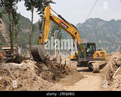 Baoding, chinesische Provinz Hebei. Aug. 2023. Ein Arbeiter fährt einen Bagger, um eine Straße im Dorf Pingyu im Laishui County in der nordchinesischen Provinz Hebei am 17. August 2023 aufzuräumen. Laishui County hat durch die Auswirkungen des Taifuns Doksuri in letzter Zeit starke Niederschläge erlitten. Die lokalen Behörden haben aktiv den Wiederaufbau nach Katastrophen durchgeführt, um die Sicherheit der Bewohner zu gewährleisten und den von Überschwemmungen betroffenen Regionen wieder auf Kurs zu bringen. Quelle: Luo Xuefeng/Xinhua/Alamy Live News Stockfoto