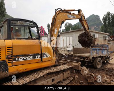 Baoding, chinesische Provinz Hebei. Aug. 2023. Ein Arbeiter fährt einen Bagger, um Schlamm im Dorf Pingyu im Laishui County in der nordchinesischen Provinz Hebei am 17. August 2023 aufzuräumen. Laishui County hat durch die Auswirkungen des Taifuns Doksuri in letzter Zeit starke Niederschläge erlitten. Die lokalen Behörden haben aktiv den Wiederaufbau nach Katastrophen durchgeführt, um die Sicherheit der Bewohner zu gewährleisten und den von Überschwemmungen betroffenen Regionen wieder auf Kurs zu bringen. Quelle: Luo Xuefeng/Xinhua/Alamy Live News Stockfoto