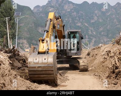 Baoding, chinesische Provinz Hebei. Aug. 2023. Ein Arbeiter fährt einen Bagger, um eine Straße im Dorf Pingyu im Laishui County in der nordchinesischen Provinz Hebei am 17. August 2023 aufzuräumen. Laishui County hat durch die Auswirkungen des Taifuns Doksuri in letzter Zeit starke Niederschläge erlitten. Die lokalen Behörden haben aktiv den Wiederaufbau nach Katastrophen durchgeführt, um die Sicherheit der Bewohner zu gewährleisten und den von Überschwemmungen betroffenen Regionen wieder auf Kurs zu bringen. Quelle: Luo Xuefeng/Xinhua/Alamy Live News Stockfoto