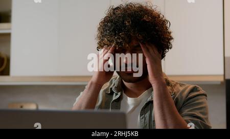 Müder arabischer Freiberufler, Geschäftsmann, der von der Hausküche aus arbeitet, leidet unter Kopfschmerzen. Kranker, erschöpfter indischer Student, der mit Laptop erschöpft war Stockfoto